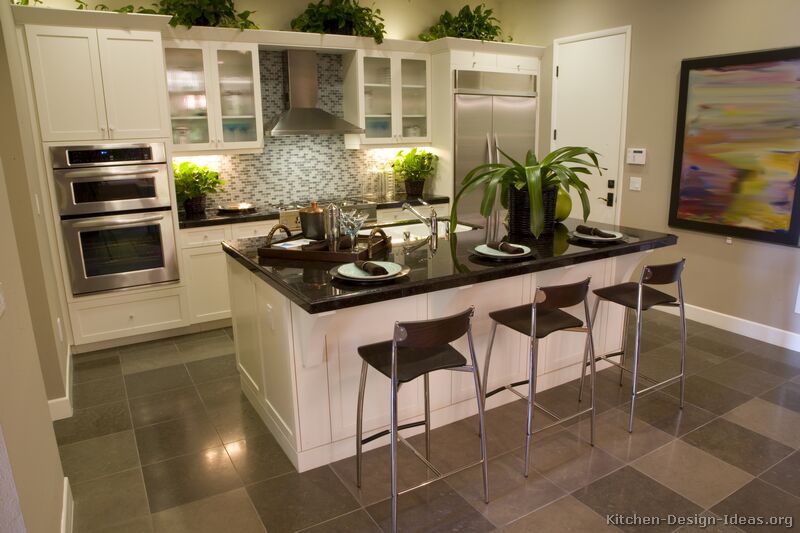 A transitional kitchen design with white cabinets, a blue glass tile backsplash, gray floors, and black countertops